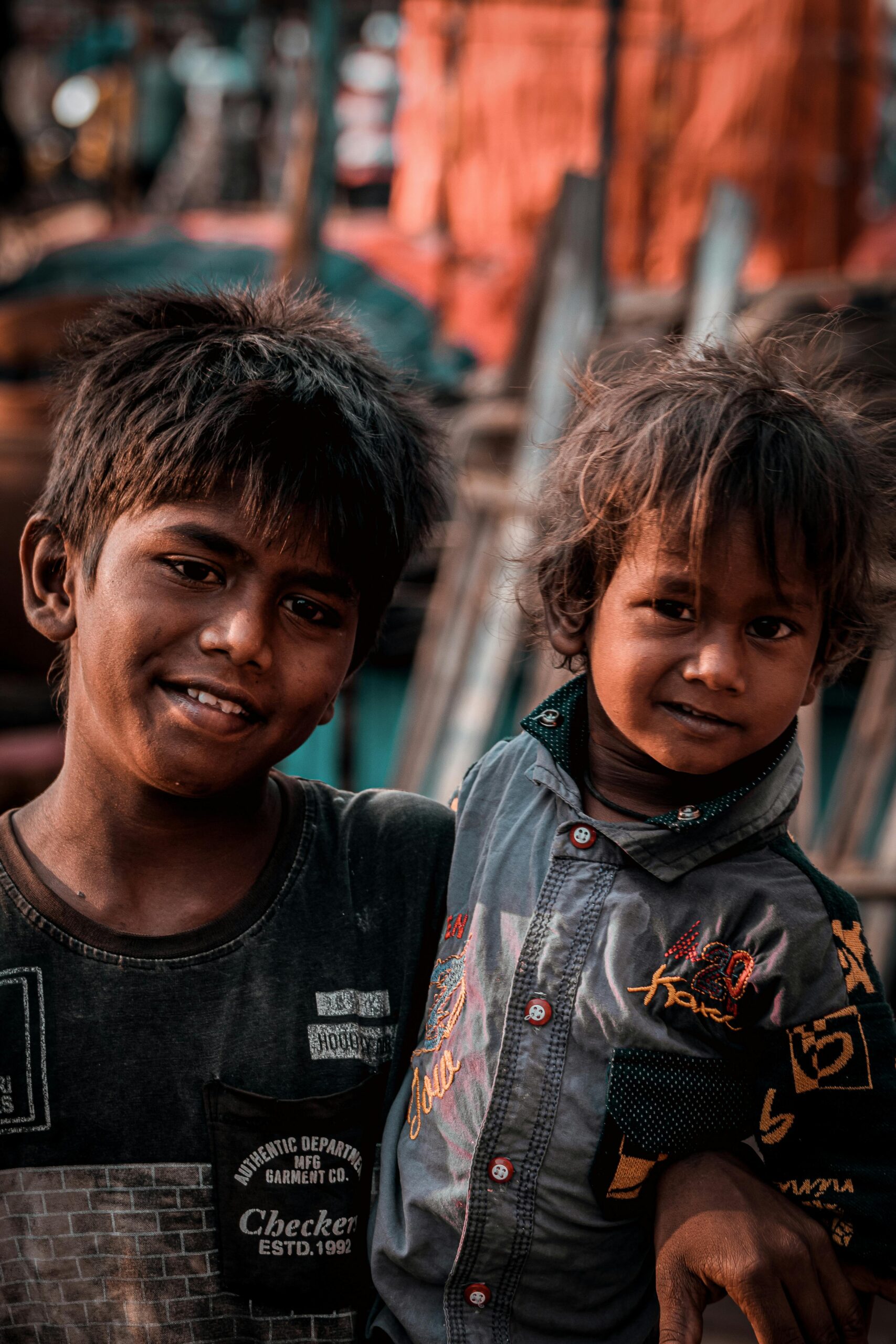 Two smiling South Asian boys in Hyderabad, India embracing each other outdoors.